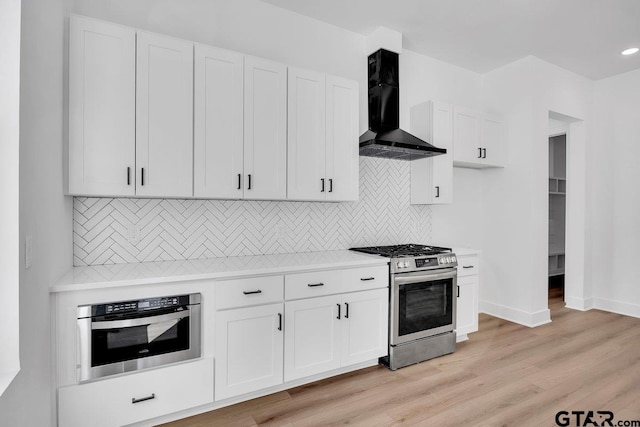 kitchen featuring white cabinetry, decorative backsplash, light hardwood / wood-style floors, stainless steel appliances, and wall chimney exhaust hood