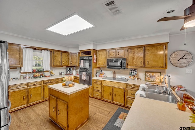 kitchen featuring sink, black appliances, ornamental molding, a center island, and light wood-type flooring