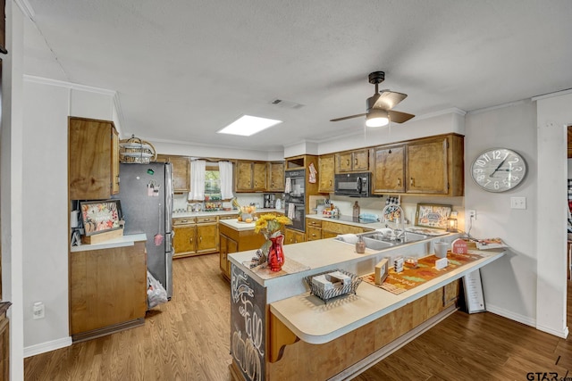 kitchen featuring ornamental molding, kitchen peninsula, black appliances, and light wood-type flooring