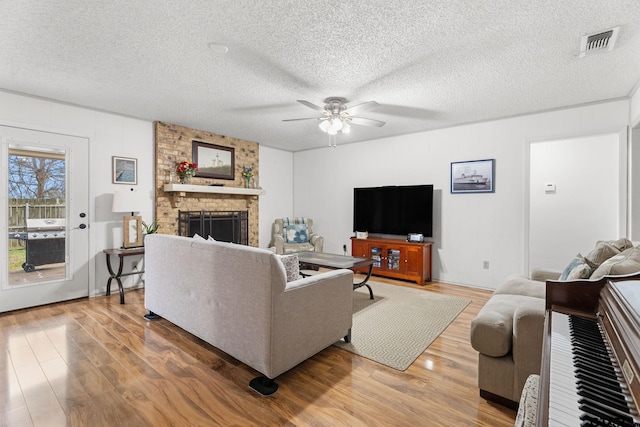 living room featuring a brick fireplace, wood-type flooring, a textured ceiling, and ceiling fan