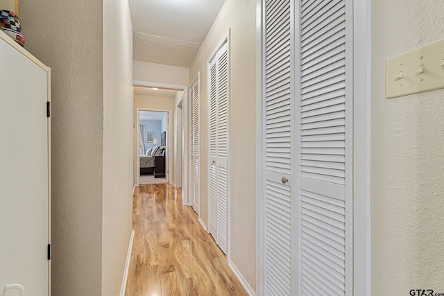 hall featuring light wood-type flooring and a textured ceiling