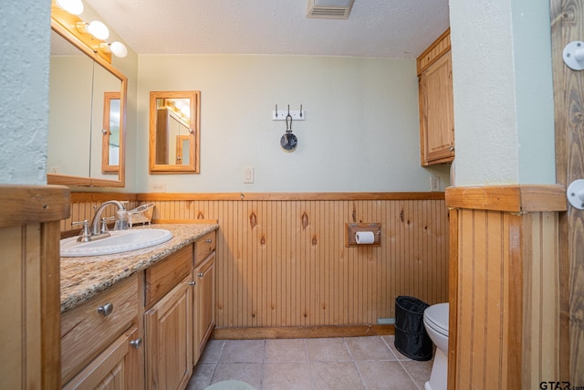 bathroom with tile patterned floors, vanity, a textured ceiling, toilet, and wood walls