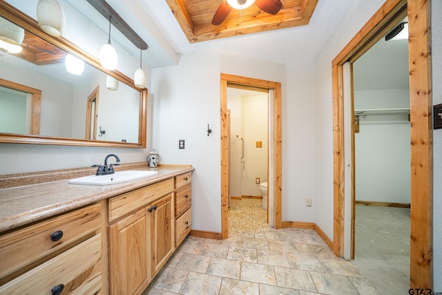 bathroom with a raised ceiling, vanity, toilet, and ceiling fan