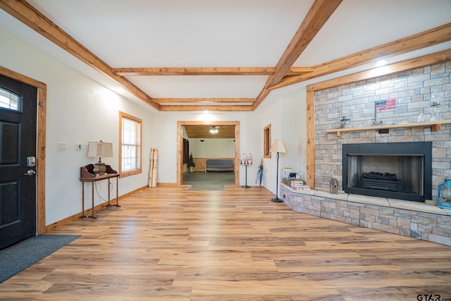 living room with beamed ceiling, light wood-type flooring, and a stone fireplace