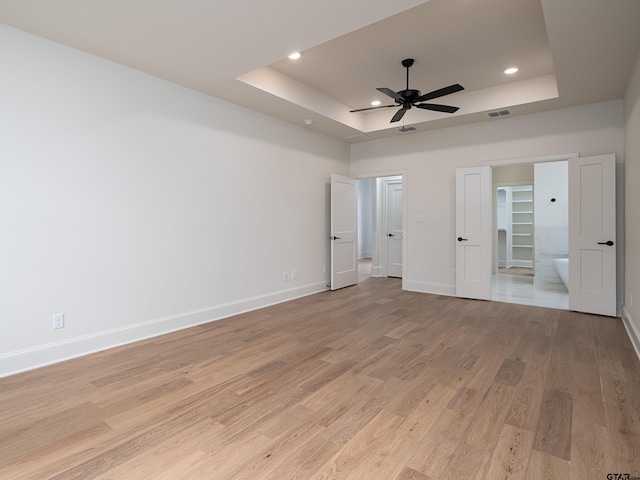 unfurnished bedroom with ensuite bath, a tray ceiling, ceiling fan, and light hardwood / wood-style flooring