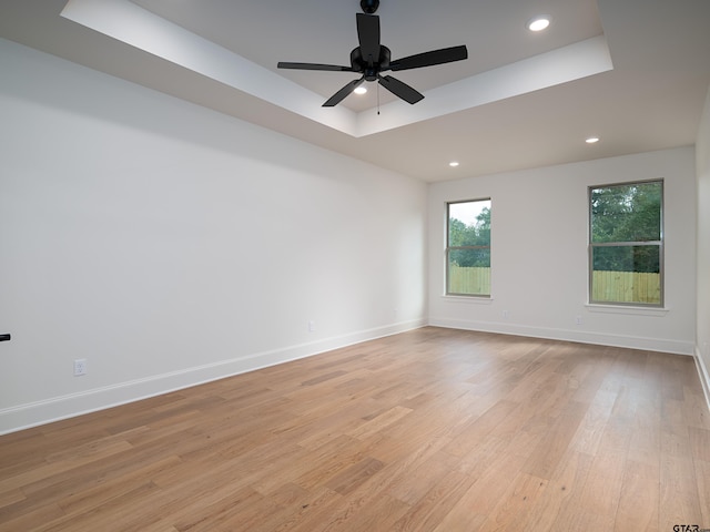 spare room with light wood-type flooring, ceiling fan, and a raised ceiling