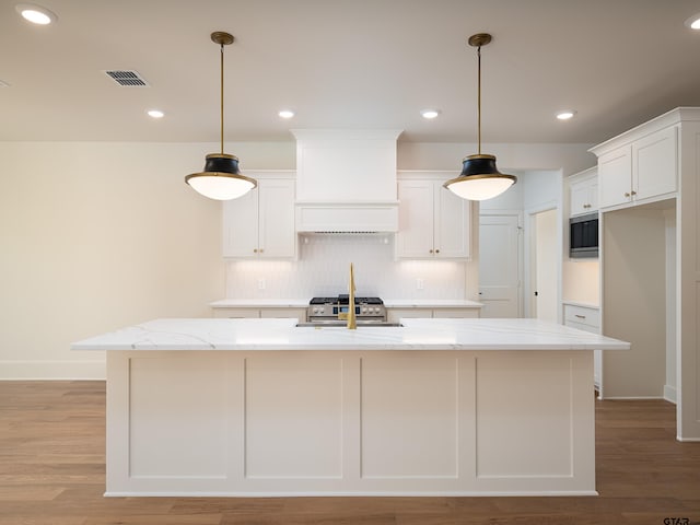 kitchen featuring white cabinets, a kitchen island with sink, light stone counters, and light hardwood / wood-style flooring