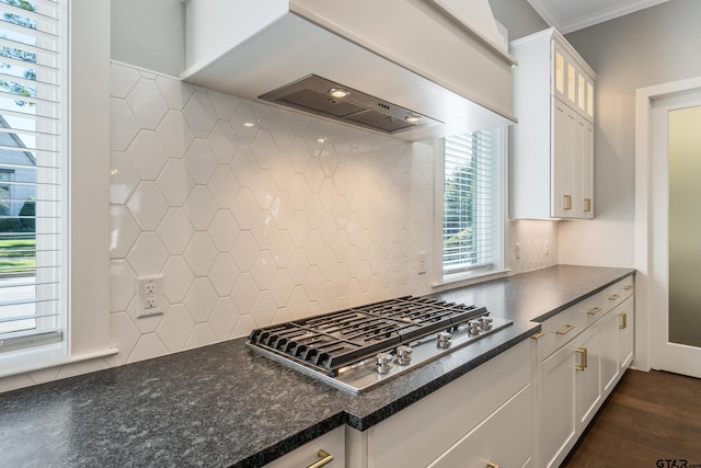 kitchen with dark wood-type flooring, wall chimney range hood, stainless steel gas cooktop, decorative backsplash, and white cabinets