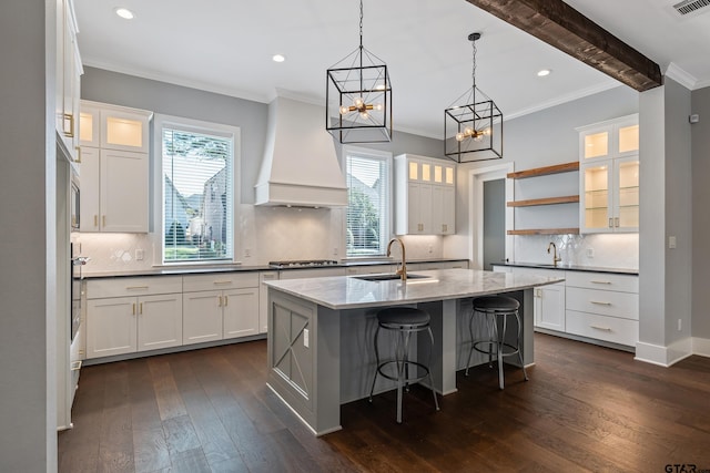 kitchen featuring dark wood-type flooring, a center island with sink, white cabinets, sink, and beam ceiling