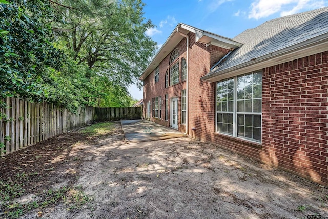 view of side of property with roof with shingles, a patio, brick siding, and a fenced backyard
