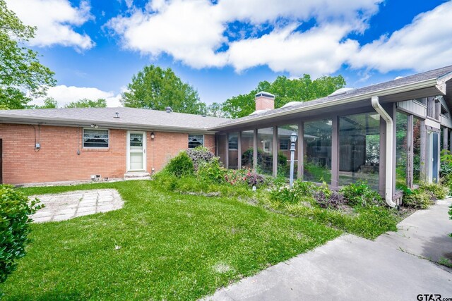 138 Drexel Dr, Sulphur Springs, TX 75482 - back of property with a chimney, brick siding, a yard, and a sunroom