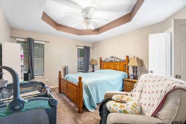 carpeted bedroom featuring ceiling fan and a tray ceiling