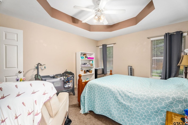 carpeted bedroom with ceiling fan and a tray ceiling