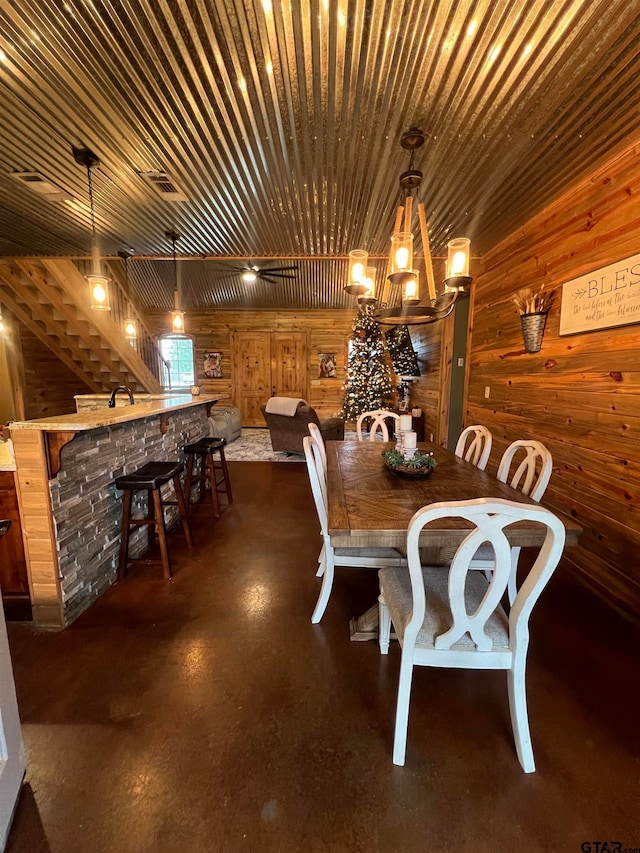 dining area featuring bar area, a notable chandelier, and wood walls