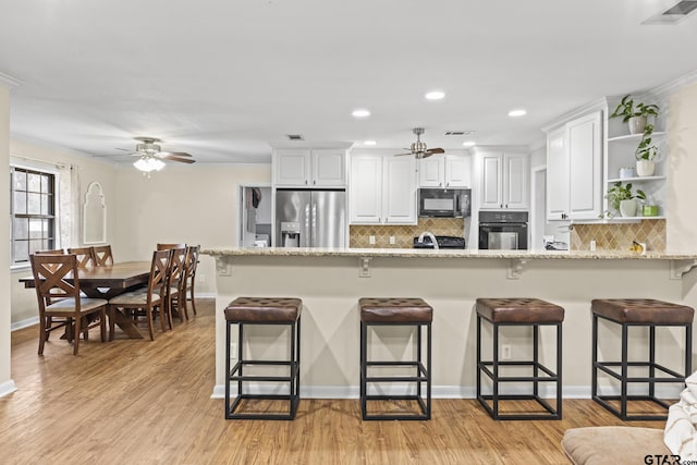 kitchen with black appliances, light wood-type flooring, light stone countertops, a breakfast bar area, and white cabinets