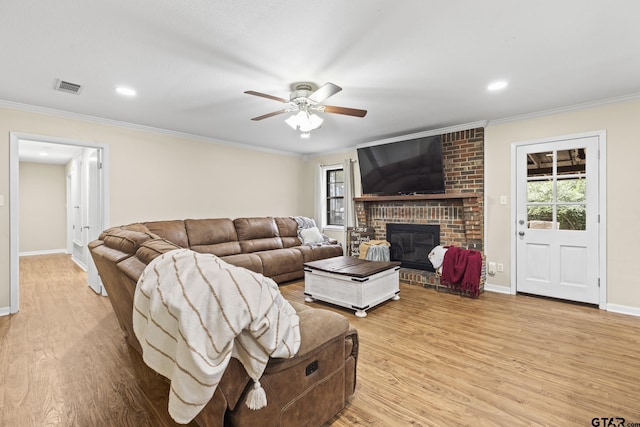 living room featuring ceiling fan, crown molding, a fireplace, and light hardwood / wood-style flooring