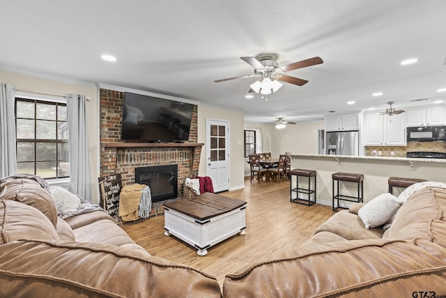 living room with a brick fireplace, ornamental molding, ceiling fan, and light wood-type flooring