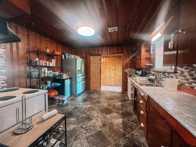 kitchen featuring backsplash, stainless steel refrigerator with ice dispenser, wooden walls, sink, and wooden ceiling