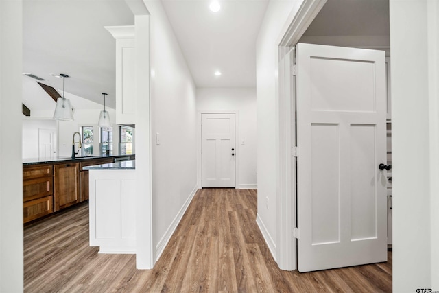 hall with sink, wood-type flooring, and vaulted ceiling