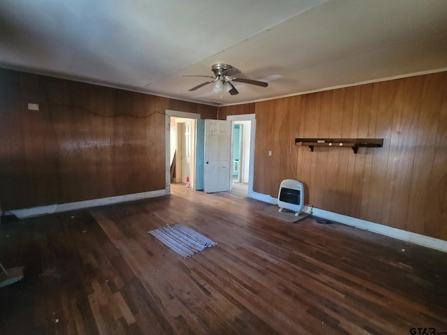 spare room featuring dark wood-type flooring, wooden walls, heating unit, and ceiling fan