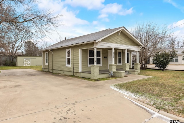 bungalow-style home featuring a porch, an outbuilding, concrete driveway, and a front lawn