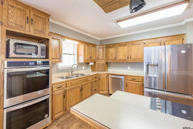 kitchen featuring crown molding, light countertops, a sink, stainless steel appliances, and light wood-style floors