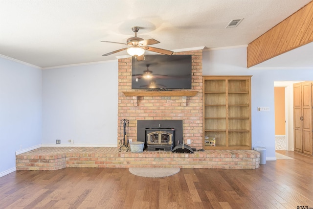unfurnished living room featuring visible vents, crown molding, ceiling fan, wood finished floors, and a wood stove