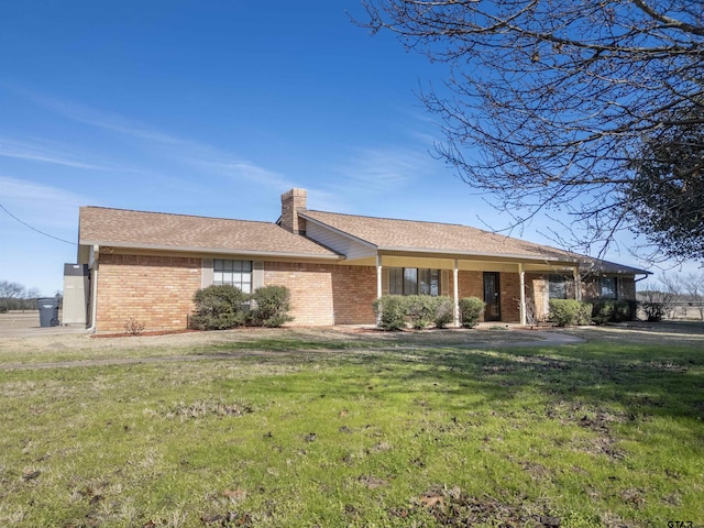 ranch-style house featuring a chimney, brick siding, and a front yard