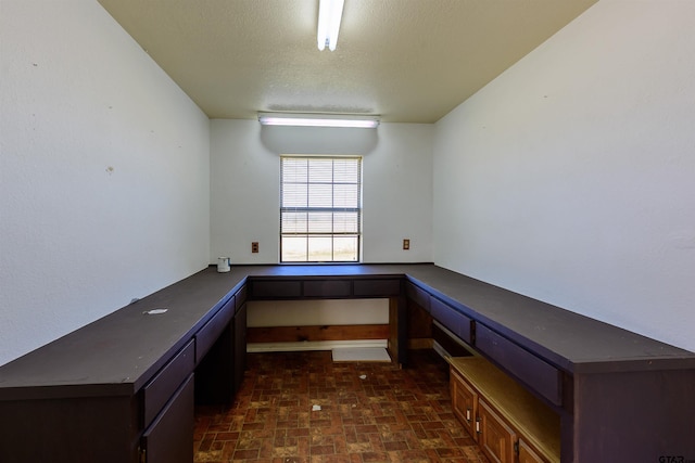 unfurnished office featuring built in desk, a textured ceiling, and brick patterned floor