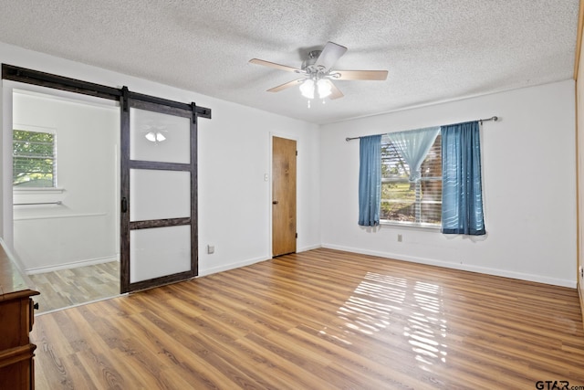 314 Cedar St, Mount Pleasant, TX 75455 - spare room featuring a textured ceiling, a barn door, baseboards, a ceiling fan, and wood finished floors