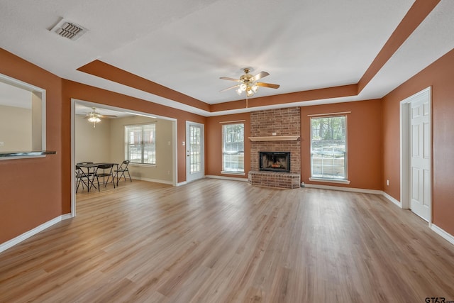 unfurnished living room with light wood-style floors, visible vents, a raised ceiling, and a ceiling fan