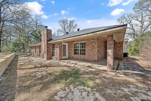 rear view of house featuring a patio, brick siding, central AC unit, and a chimney