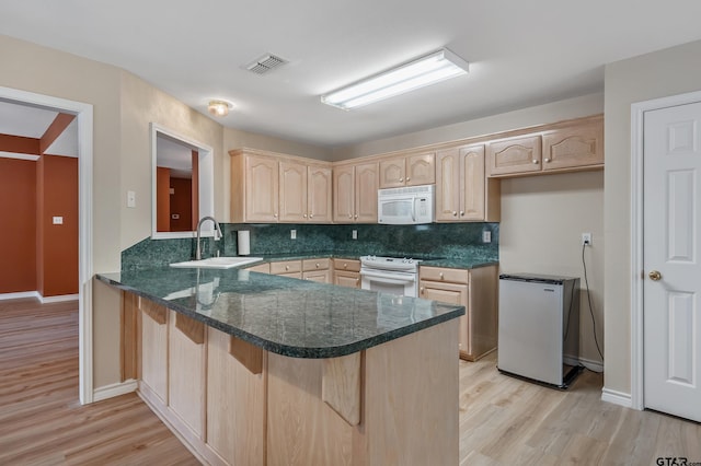 kitchen with white appliances, visible vents, a peninsula, a sink, and light brown cabinetry