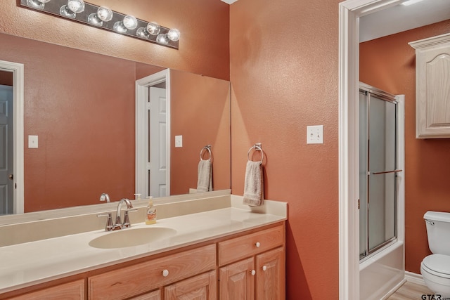 full bath with toilet, vanity, and bath / shower combo with glass door