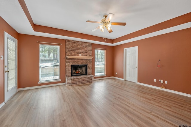 unfurnished living room with a wealth of natural light, a raised ceiling, light wood-style floors, and ceiling fan
