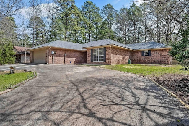 ranch-style house with a front yard, driveway, roof with shingles, an attached garage, and brick siding