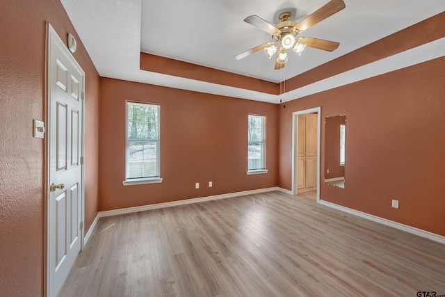 empty room with a raised ceiling, light wood-style flooring, a healthy amount of sunlight, and ceiling fan