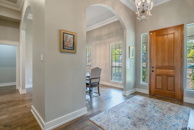 entryway featuring ornamental molding, a towering ceiling, dark wood-type flooring, and a notable chandelier