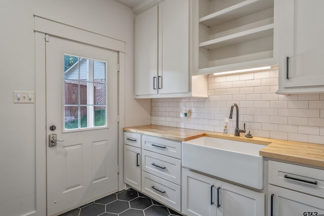 kitchen with white cabinetry, sink, wood counters, backsplash, and dark tile patterned flooring