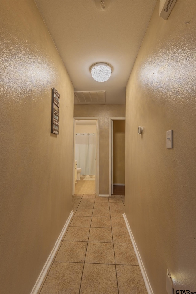 corridor with light tile patterned floors, visible vents, and baseboards
