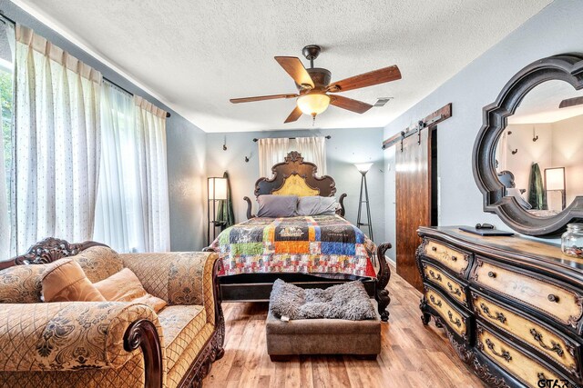 902 S Florey, Mount Pleasant, TX 75455 - bedroom featuring a barn door, wood finished floors, a textured ceiling, and ceiling fan
