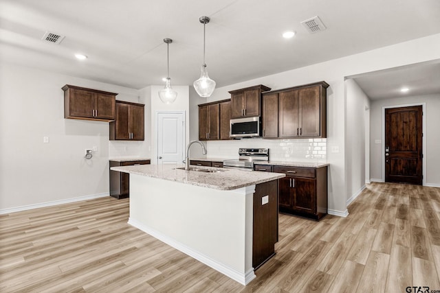 kitchen featuring light stone countertops, sink, hanging light fixtures, a kitchen island with sink, and appliances with stainless steel finishes