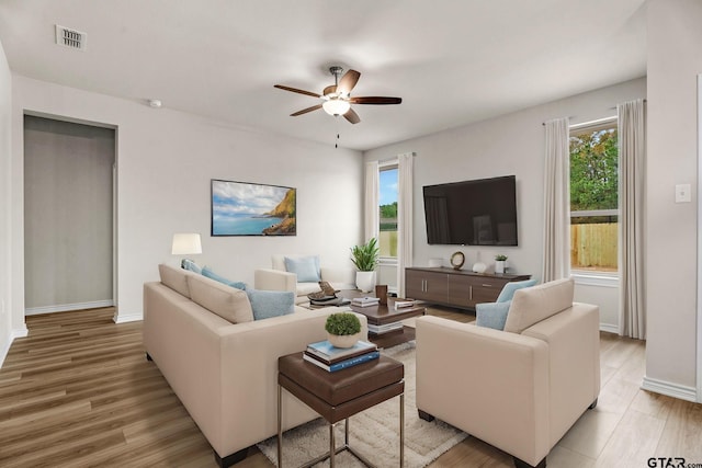 living room with light wood-type flooring, ceiling fan, and a healthy amount of sunlight