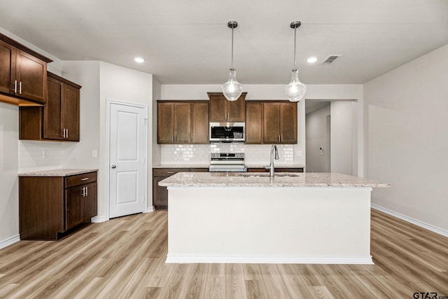 kitchen featuring light stone countertops, sink, a kitchen island with sink, and appliances with stainless steel finishes