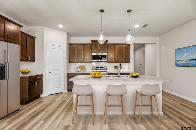 kitchen featuring sink, an island with sink, stainless steel appliances, and decorative light fixtures