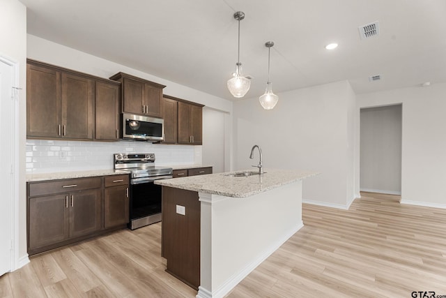 kitchen with dark brown cabinetry, light stone countertops, sink, stainless steel appliances, and a kitchen island with sink