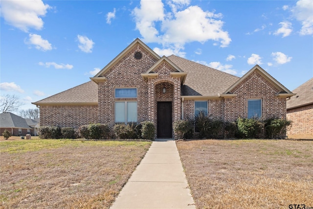 traditional-style house with brick siding, a front yard, and a shingled roof