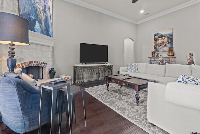 living room featuring ceiling fan, ornamental molding, a stone fireplace, wood finished floors, and arched walkways