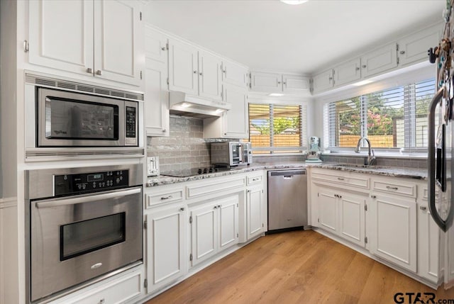 2733 Rockbridge Rd, Tyler, TX 75701 - kitchen with stainless steel appliances, under cabinet range hood, light wood-style flooring, light stone counters, and white cabinetry