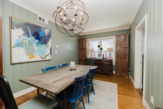 dining area with baseboards, visible vents, light wood finished floors, ornamental molding, and a chandelier